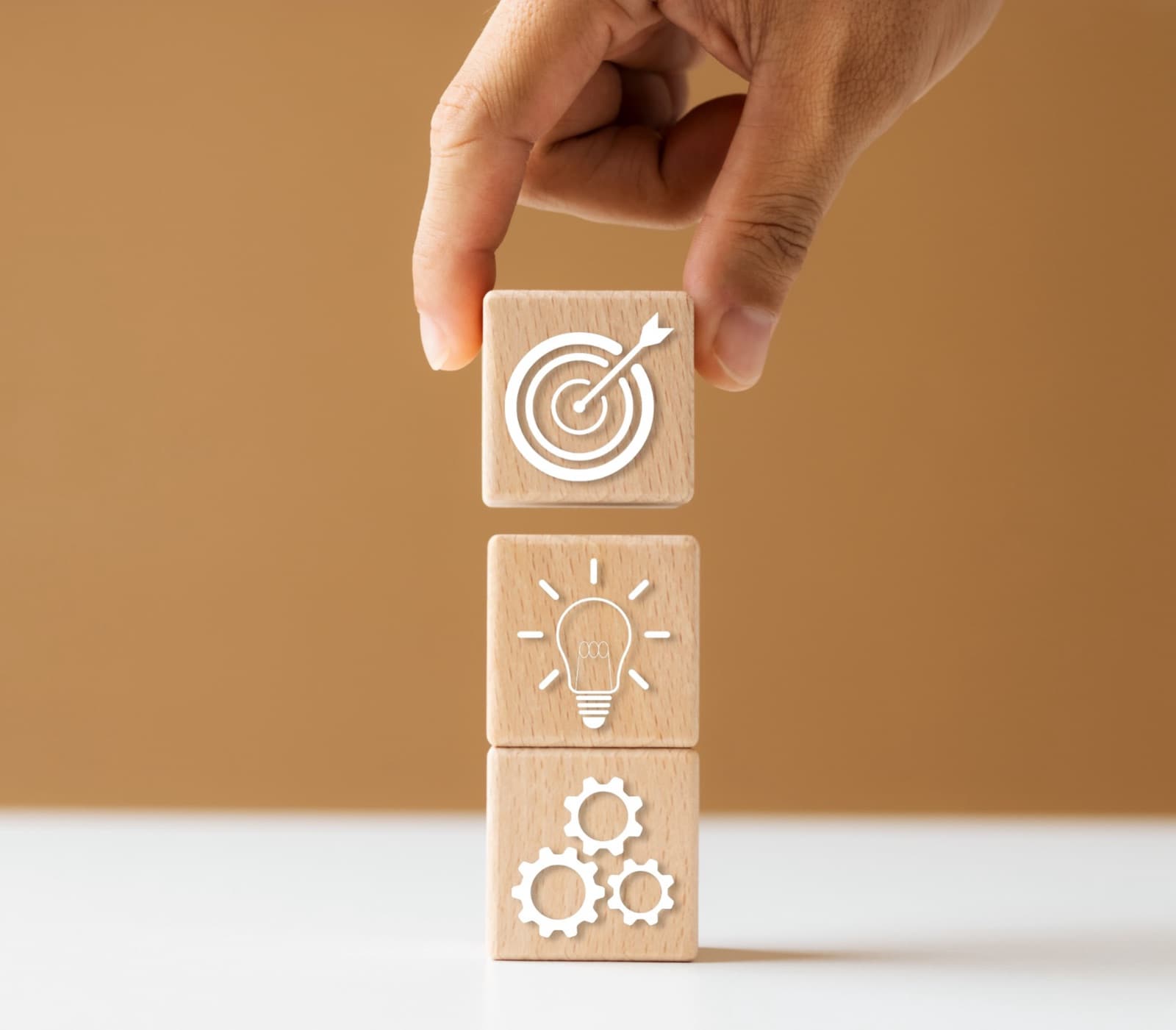 Hand stacking wooden blocks symbolizing goals, ideas, and actions